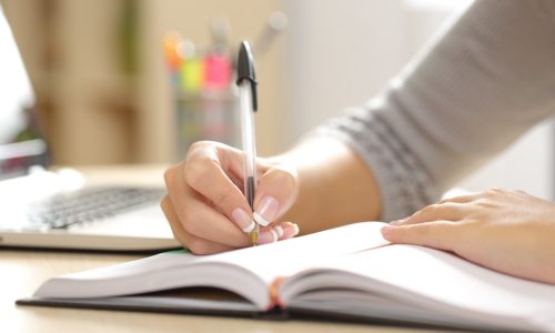 Close up of a woman hand writing in an agenda on a desk at home or office