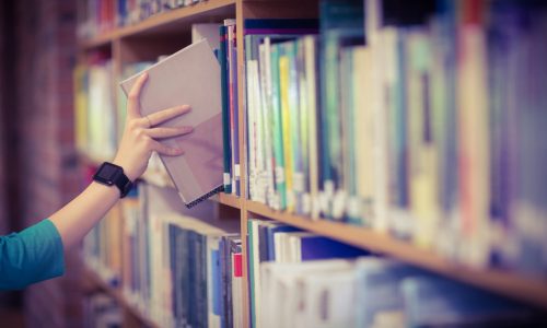 Students hand with smartwatch picking book from bookshelf at the university